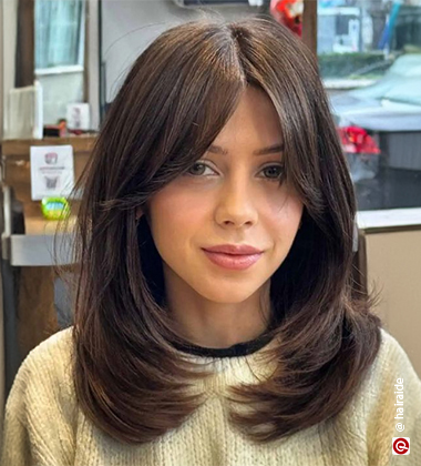 woman in a beige sweater and curtain bangs